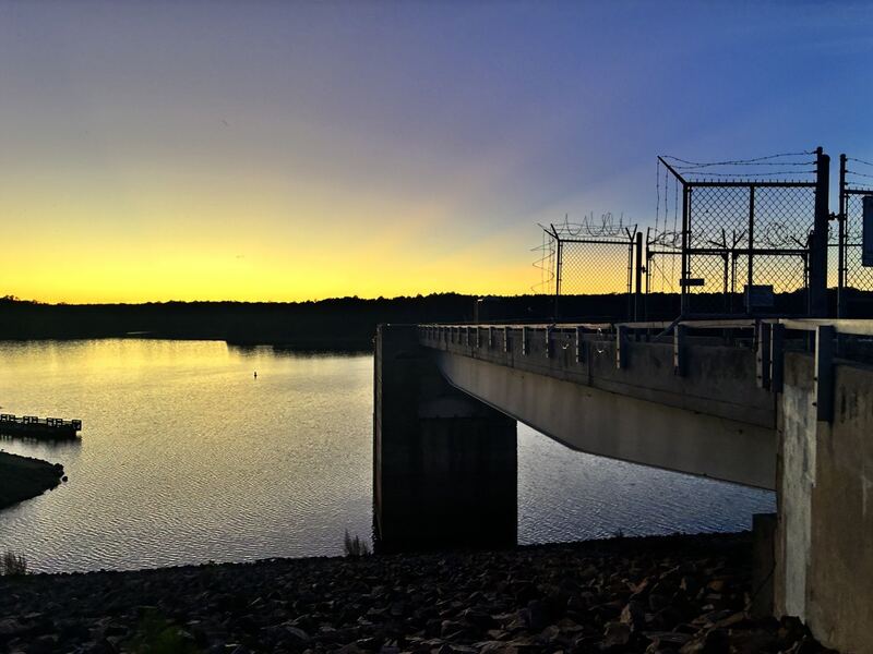 The dam structure silhouetted against the last warm light over Falls Lake.